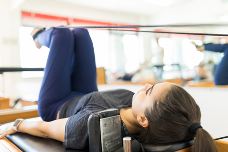 Full length of body conscious woman exercising on pilates reformer machine in gymの写真素材