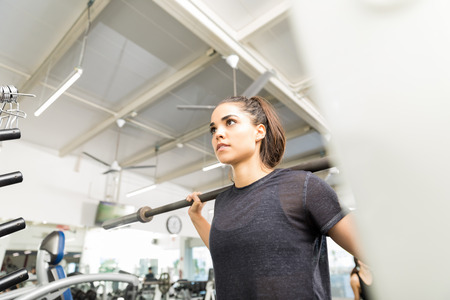 Low angle view of athletic woman exercising with empty barbell in gym
