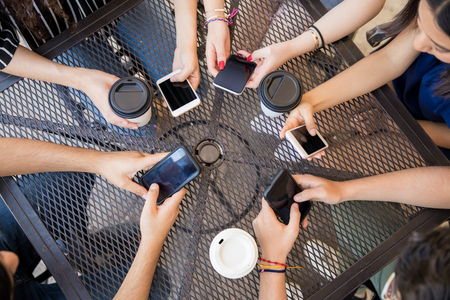 Top view of young friends hands using mobile phones at cafeの写真素材