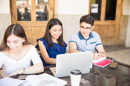 Smiling young girl sitting at coffee shop with friends using laptopの写真素材