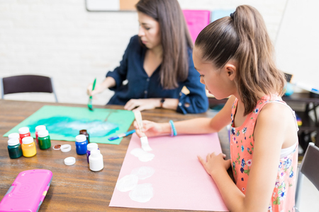 Girl and mother coloring drawing papers at table in houseの写真素材