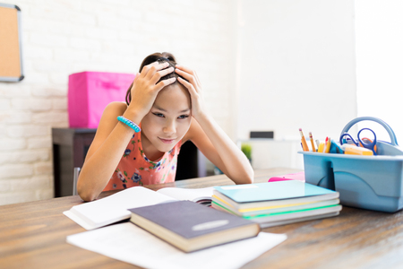 Stressed female student with head in hands sitting at table in houseの写真素材