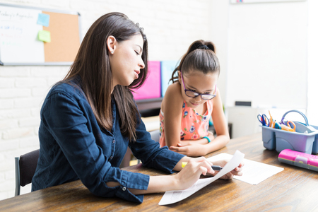 Mid adult female tutor helping girl with homework at table in houseの写真素材