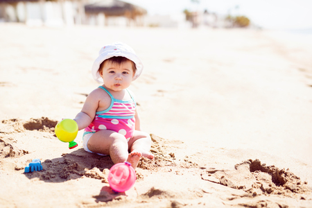 Portrait of a pretty baby girl wearing a hat and a swimsuit and playing in the beach on a sunny morningの写真素材
