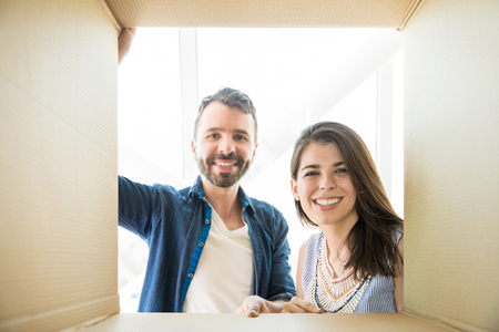 Portrait of mid adult couple smiling while looking into cardboard box in new homeの写真素材