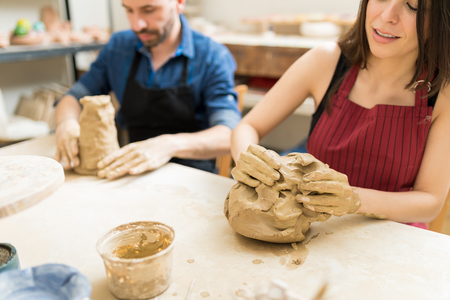 Mid adult woman and man preparing clay to make pottery at table in workshopの写真素材