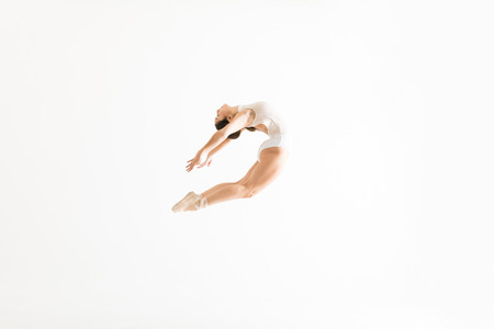 Young female ballet dancer performing high jump and backbend on white backgroundの写真素材