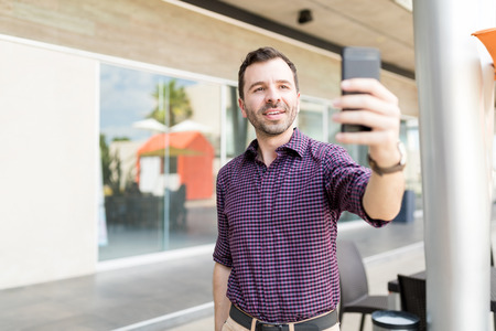 Mid adult man taking self portrait using mobile phone in shopping mallの写真素材
