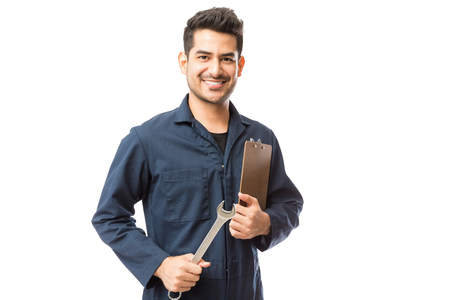 Portrait of smiling male repairman holding wrench and clipboard over white backgroundの写真素材