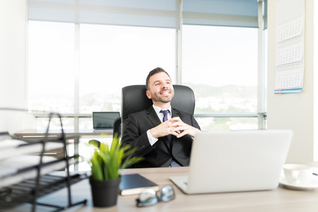 Hispanic executive manager thinking about something good while sitting in officeの写真素材