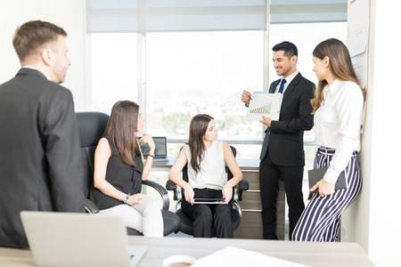 Marketing manager showing work results on graph to team during meeting in officeの写真素材