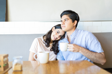 Beautiful young woman resting head on man's shoulder while sitting in cafeの写真素材