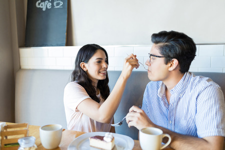 Caring partner feeding cheesecake to lover while hanging out in cafeの写真素材