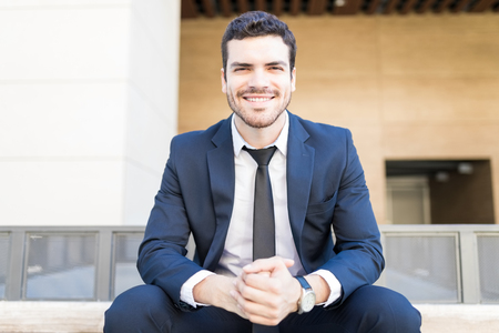 Portrait of smiling corporate manager sitting with hands clasped outside officeの写真素材