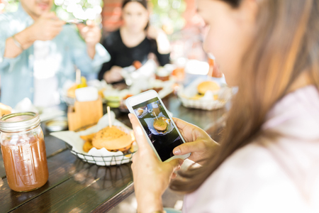 Woman photographing tempting burger on smartphone to upload on social mediaの写真素材