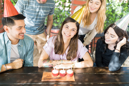 Smiling and attractive birthday woman with cupcakes surrounded by friends at restaurantの写真素材
