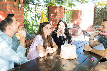 Male and female friends blowing party horns for woman during birthday celebration at restaurantの写真素材