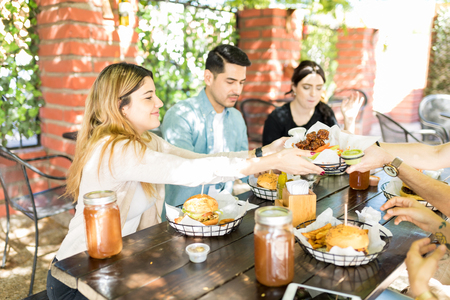 Young woman passing cooked meat to friend during social gathering at restaurant