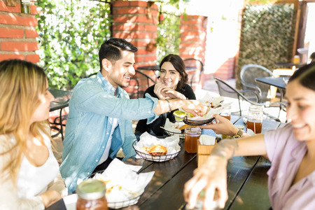 Smiling attractive man taking food from basket while enjoying party with friends at burger shopの写真素材