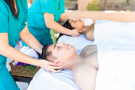 Masseuses giving head massage to young man and woman in healthcare salonの写真素材