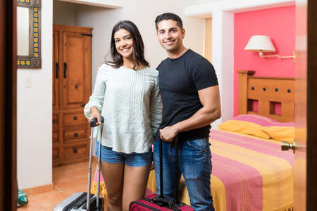 Portrait of smiling couple with luggage standing in colorful room at honeymoon resortの写真素材