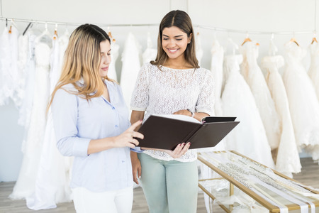 Beautiful saleswoman showing catalog of bridal collection to client in boutiqueの写真素材