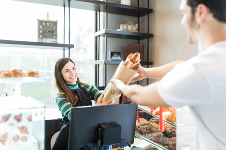 Smiling saleswoman giving bag of baguettes to male customer in storeの写真素材
