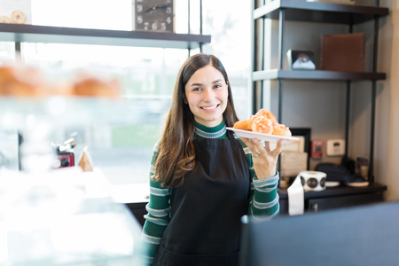 Portrait of charming saleswoman holding plate of pastries in store
