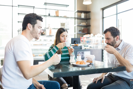 Male and female friends enjoying coffee and chouxs at table in cafe