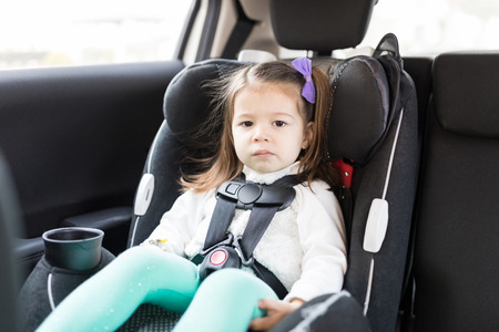 Adorable female child secured with seat belts in car