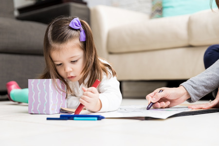 Pretty child and mother using crayons to draw on paper in living roomの写真素材