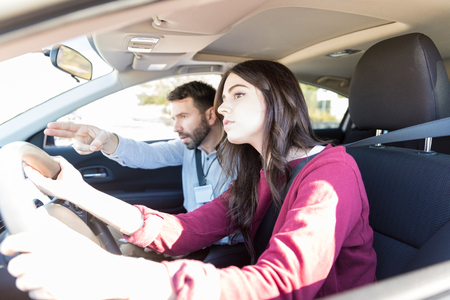 Driving teacher showing direction to young female student during driving test