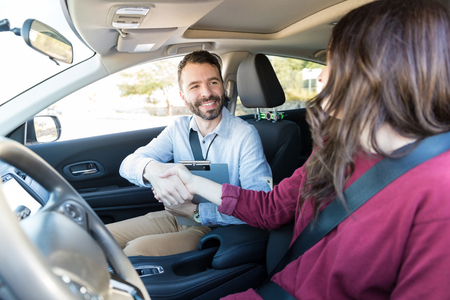Confident instructor shaking hands with driver to be in car during training session