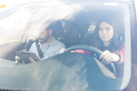 Cute woman concentrating while driving by instructor in car seen through windshield