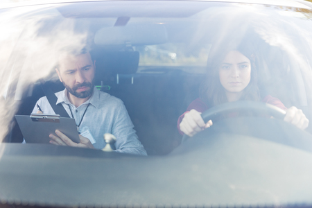 Hispanic instructor taking test of woman sitting on driver's seatの写真素材