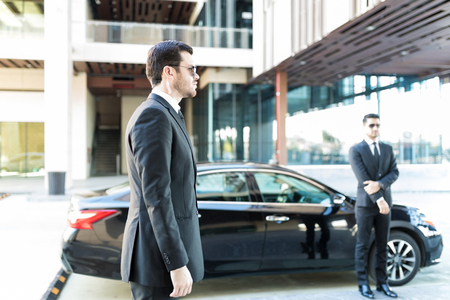 Executive protection agents standing by car while doing their duty in cityの写真素材
