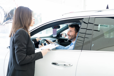 Professional salesperson and buyer talking about car specs and price at showroomの写真素材