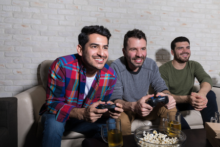 Smiling men playing electronic games and spending leisure time together at homeの写真素材