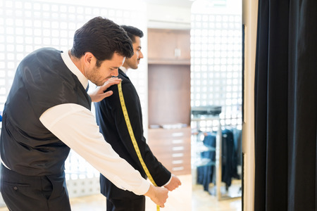 Young tailor measuring sleeve of suit worn by customer at rental storeの写真素材