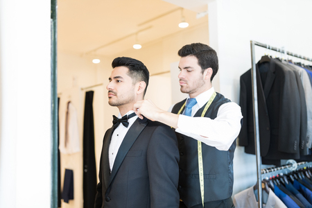 Rental shop owner providing service to customer by assisting him with bow tieの写真素材