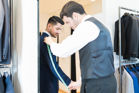 Skilled male tailor measuring arm length of client at clothing storeの写真素材