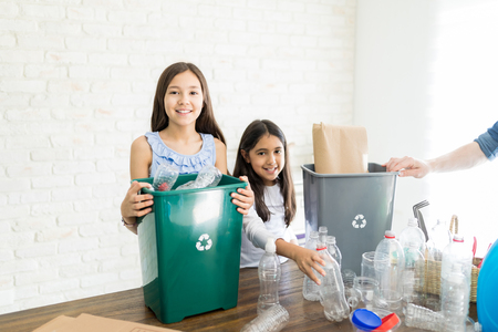 Smiling eco-friendly siblings with plastic trash at homeの写真素材