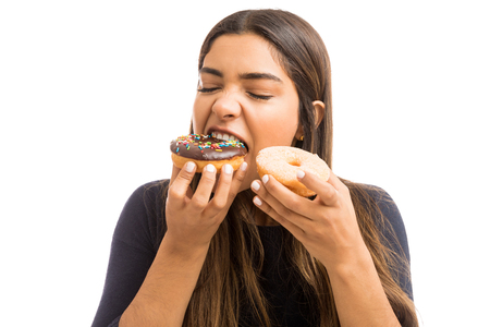 Beautiful young woman with eyes closed biting piece of chocolate donut on white backgroundの写真素材
