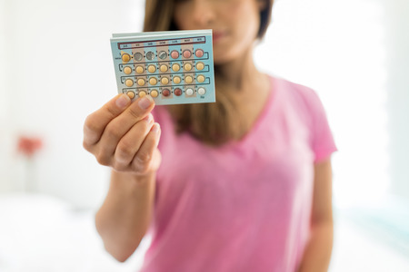 Midsection of woman holding birth control blister pack at homeの写真素材
