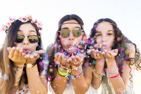 Closeup of beautiful young women blowing confetti while enjoying music festivalの写真素材