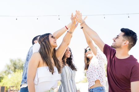 Happy friends with raised arms cheering for their friendship with high-five during summer weekendの写真素材
