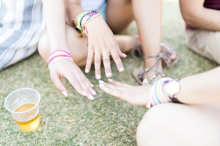 Cropped image of female friends matching painted nails while sitting on field during summerの写真素材