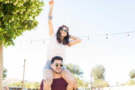Attractive woman dancing to music while sitting on shoulders of boyfriend at outdoor partyの写真素材