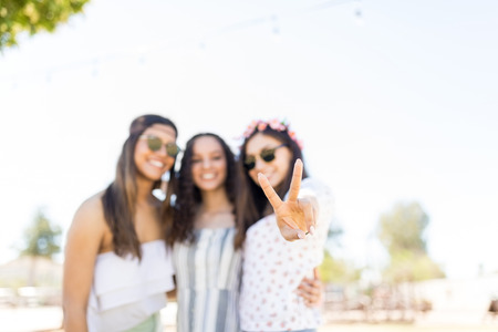 Woman showing victory gesture while posing with best friends at music festivalの写真素材