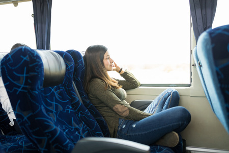 Thoughtful woman sitting comfortably on seat by window in busの写真素材